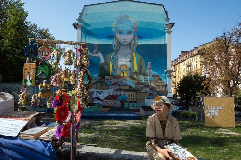 A street vendor sells goods in front of a mural painted on building in Kyiv on Sept. 19, 2015.