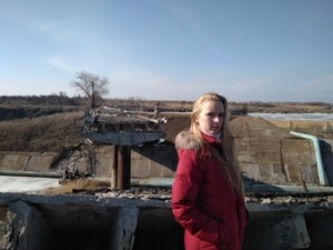 Anna Shapkina from Pavlopil, a village of 600 people located just 30 kilometers northeast of the Azov Sea port city of Mariupol, poses near the ruined bridge in her hometown. (tolerspace.org.ua)