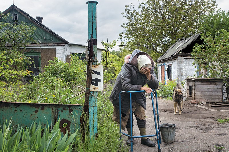 An elderly woman, Sofiya Tolmacheva, cries among damaged houses in the front-line town of Pisky on May 15. Tolmacheva is one of the few residents remaining in the town, unable to flee because she has to care for her disabled son. Another of her sons, injured in shelling, has since gone missing. She also cares for a dog left in the town by her neighbor. 