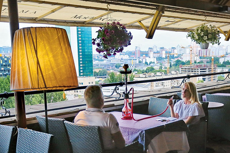 Visitors of the Panorama restaurant in Kyiv smoke hookah at a terrace with a city view on June 12. 