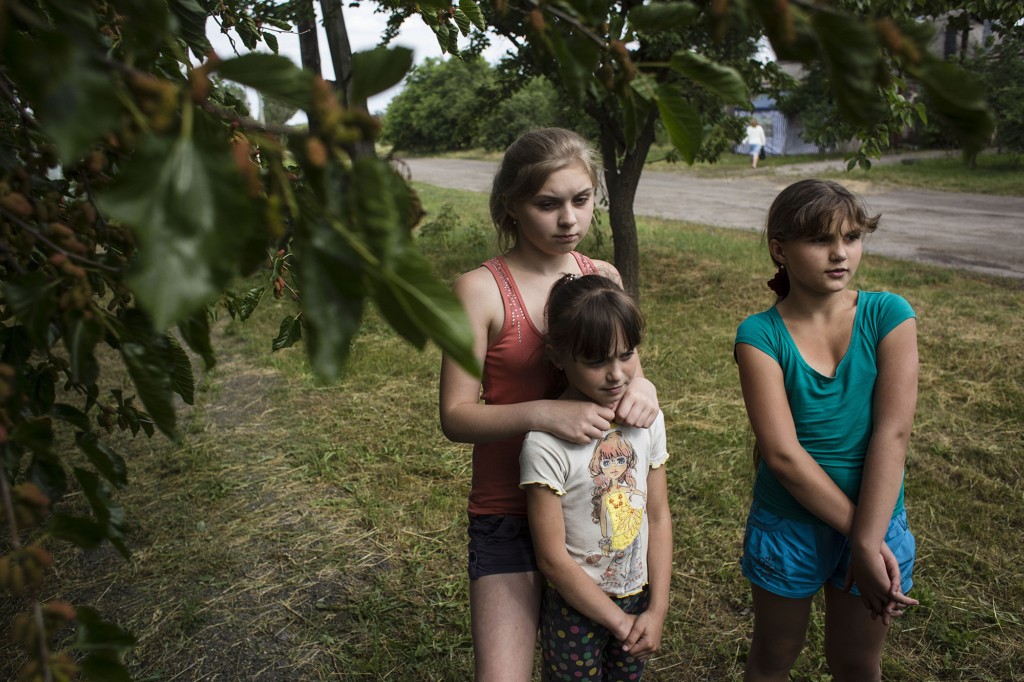 Sisters Lyuba and Sonia Pavlovy and their friend Sophia stand by their house in Krymske, Luhansk Oblast. 