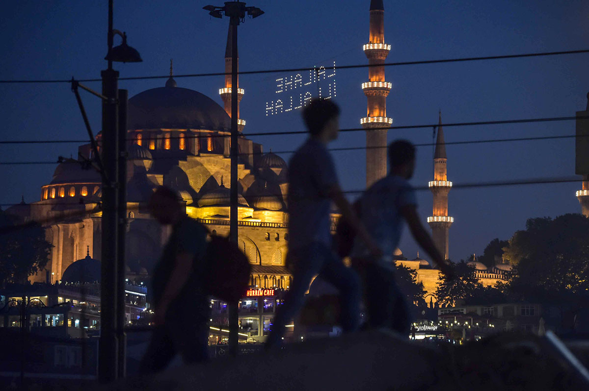 Pedestrians walk across the Galata Bridge in Eminonu District in Istanbul on June 20, with the Suleymaniye Mosque in the background. 